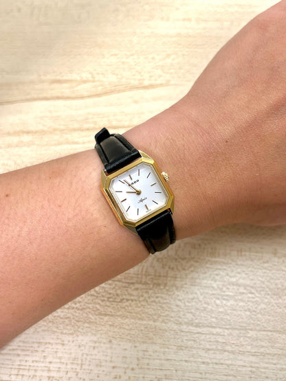 Gold Rado Women's Luxurious watch with a black strap on a wrist against a beige background