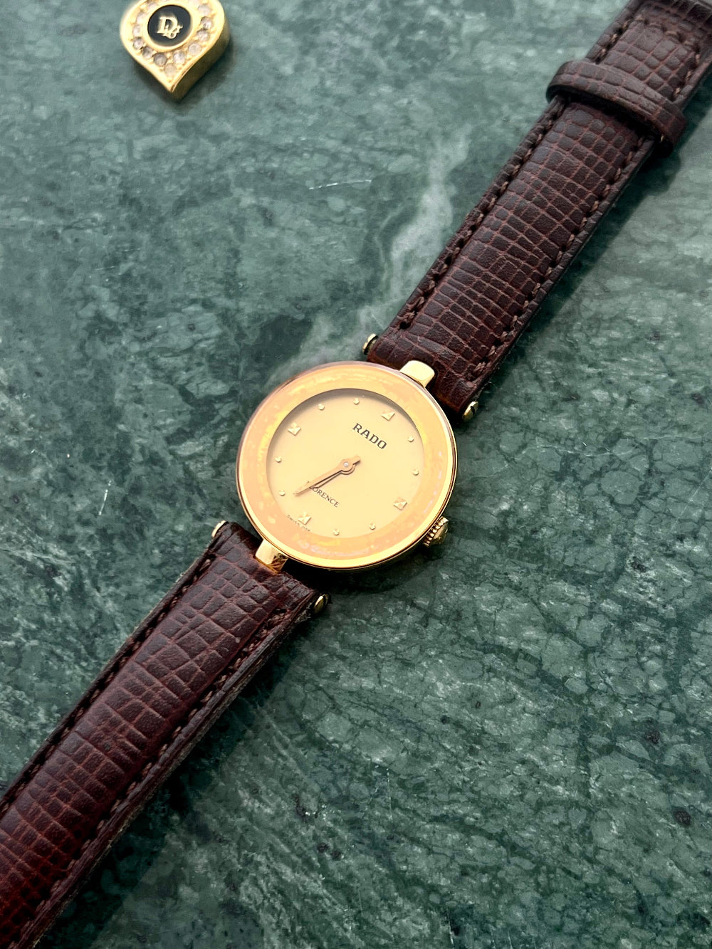 Gold Rado ladies watch in NZ with a brown leather strap on a green marble surface