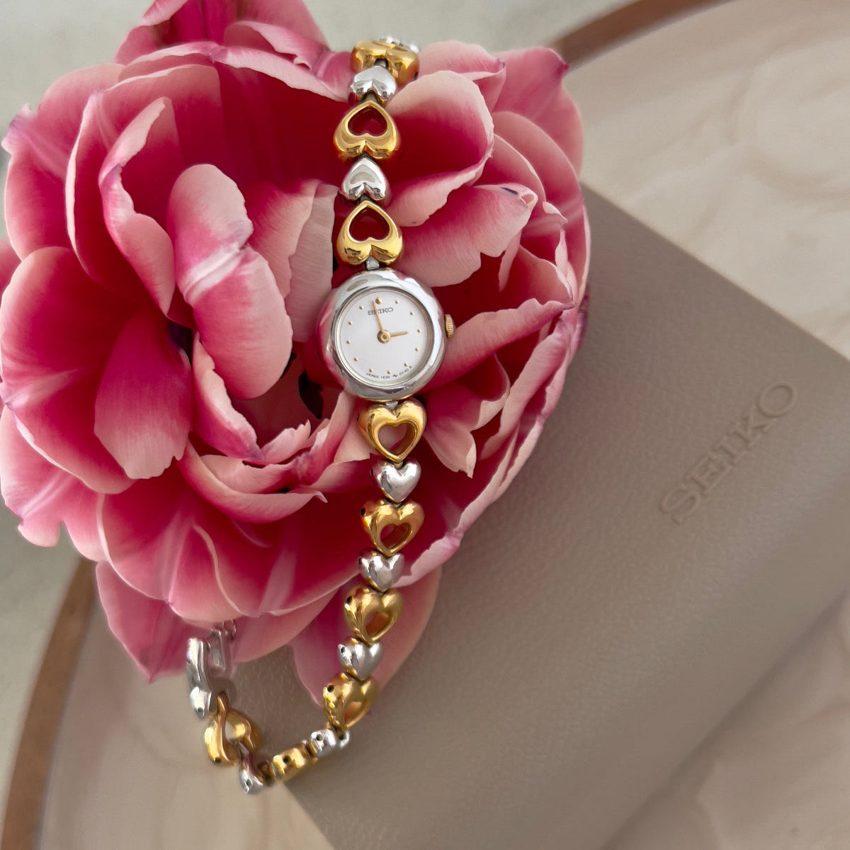 Seiko Ladies Luxury Watch with heart-shaped beads on a pink rose against a beige background
