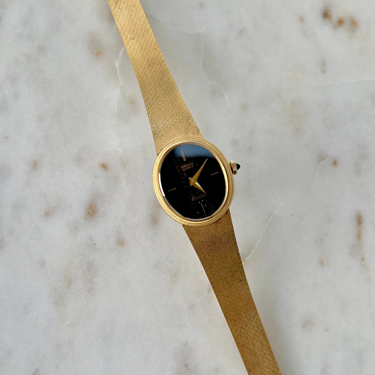Seiko Exceline Gold watch with a black face on a marble surface