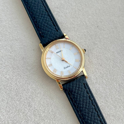 Seiko Exceline Wristwatch with black strap and gold case on a light gray background