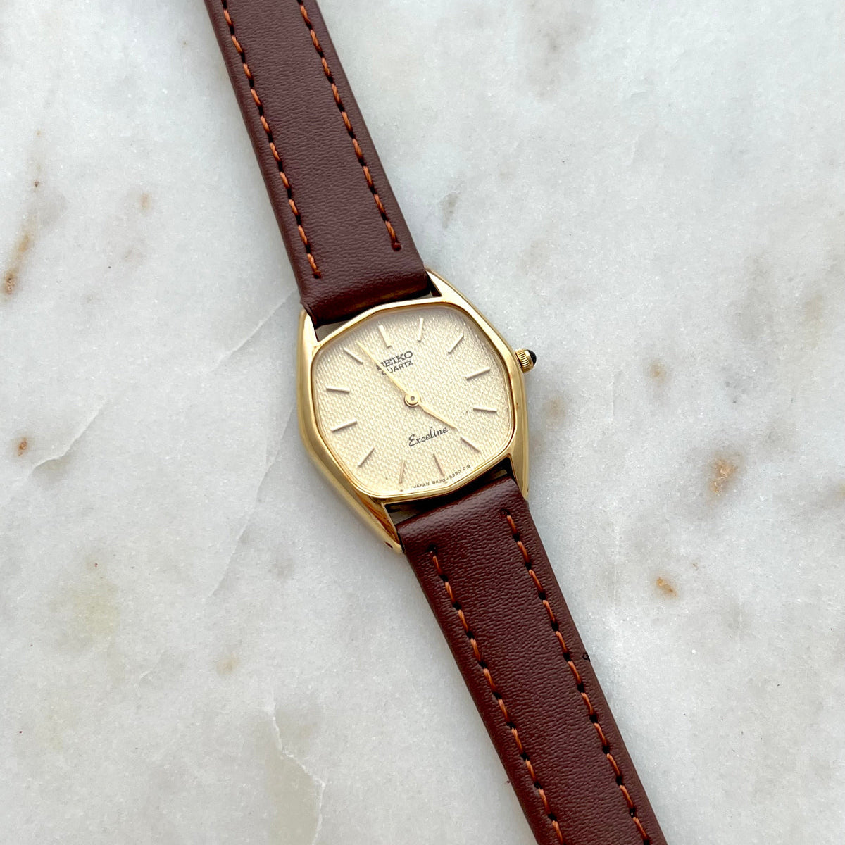 Gold Seiko Exceline watch with a brown leather strap on a marble surface