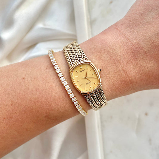 Gold watch and bracelet on a wrist with a white background