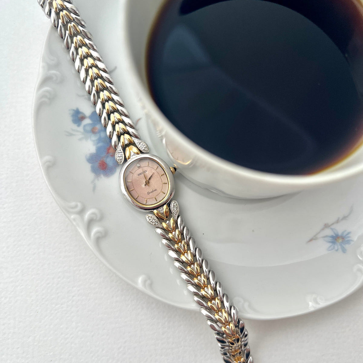 Seiko Exceline Two Tone watch with braided strap on a saucer next to a cup of coffee
