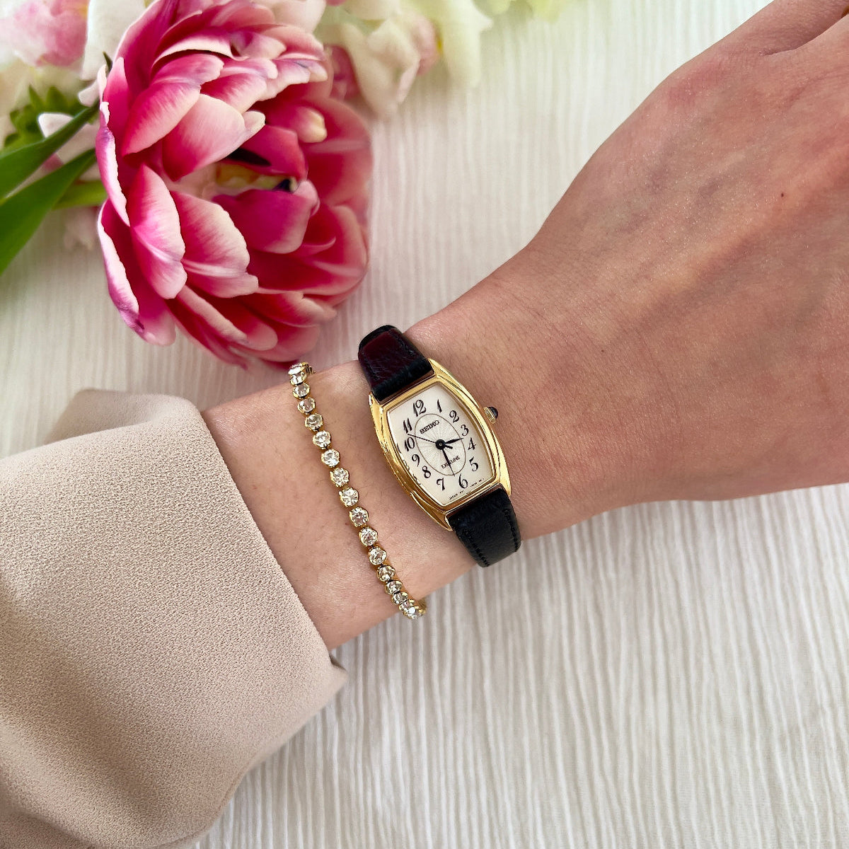 Gold Seiko Woman's watch on a wrist with pink flowers in the background