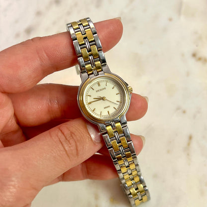 Two-tone Seiko Exceline watch held in a hand against a light background