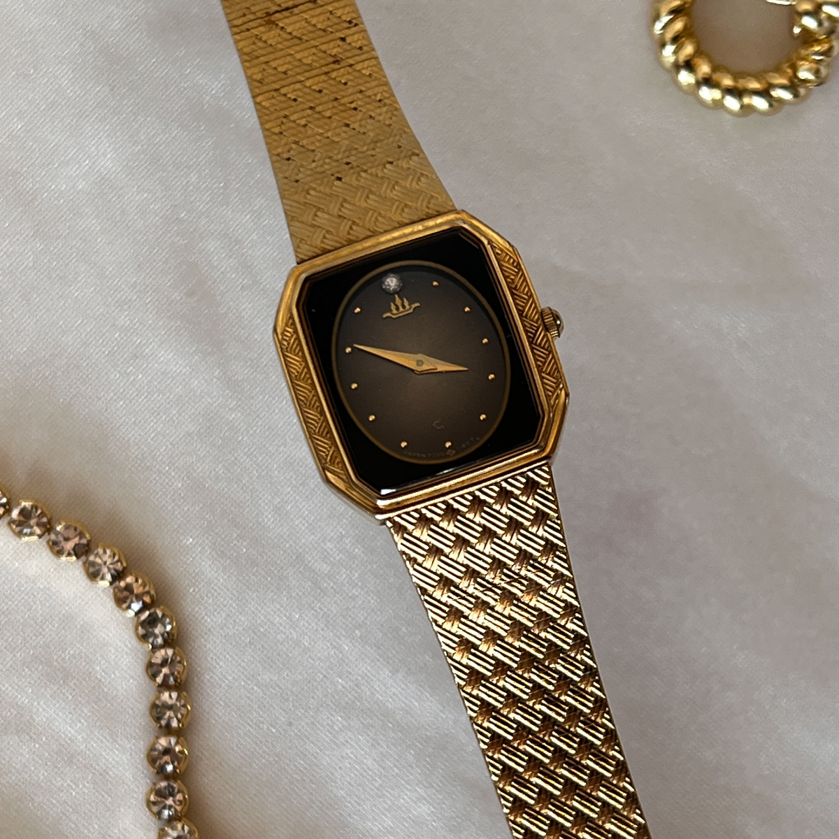 A Seiko Galaxy women's watch with a deep black burst dial and a rich gold-tone hexagonal case. The watch has a woven mesh bracelet, gold hands, and a crystal marker on the 12 position.