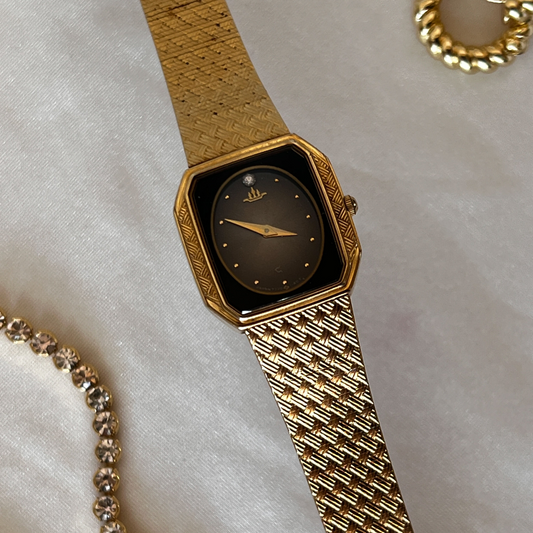 A Seiko Galaxy women's watch with a deep black burst dial and a rich gold-tone hexagonal case. The watch has a woven mesh bracelet, gold hands, and a crystal marker on the 12 position.