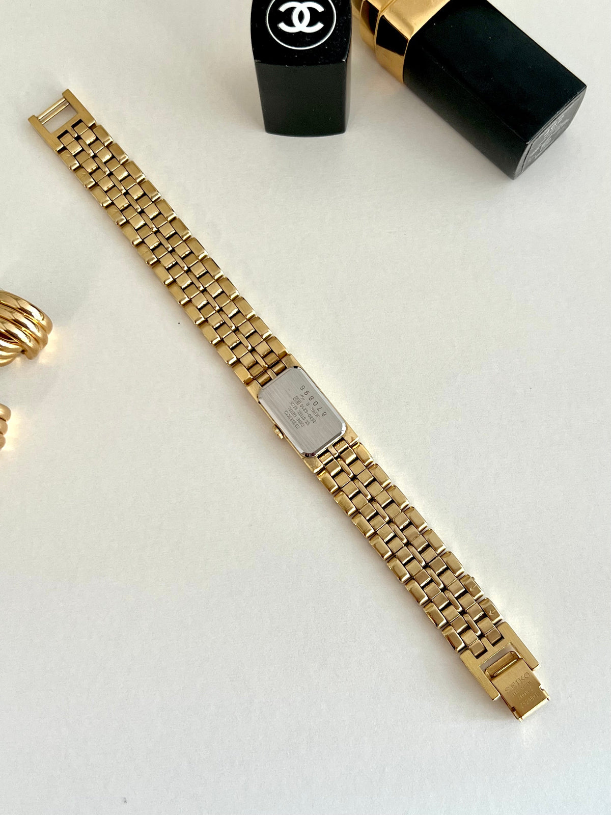 Seiko Gold watch with Bamboo Textured Bracelet strap on a white surface with a Chanel lip stick in the background