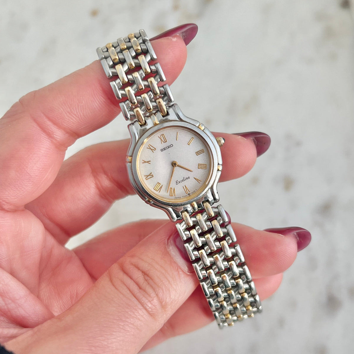 Silver Seiko watch with a chain strap held by a hand against a blurred background