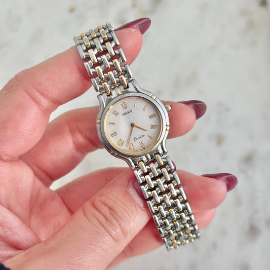 Silver Seiko watch with a chain strap held by a hand against a blurred background