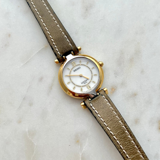 Seiko Lucent Watch with a gold case and beige leather strap on a marble surface