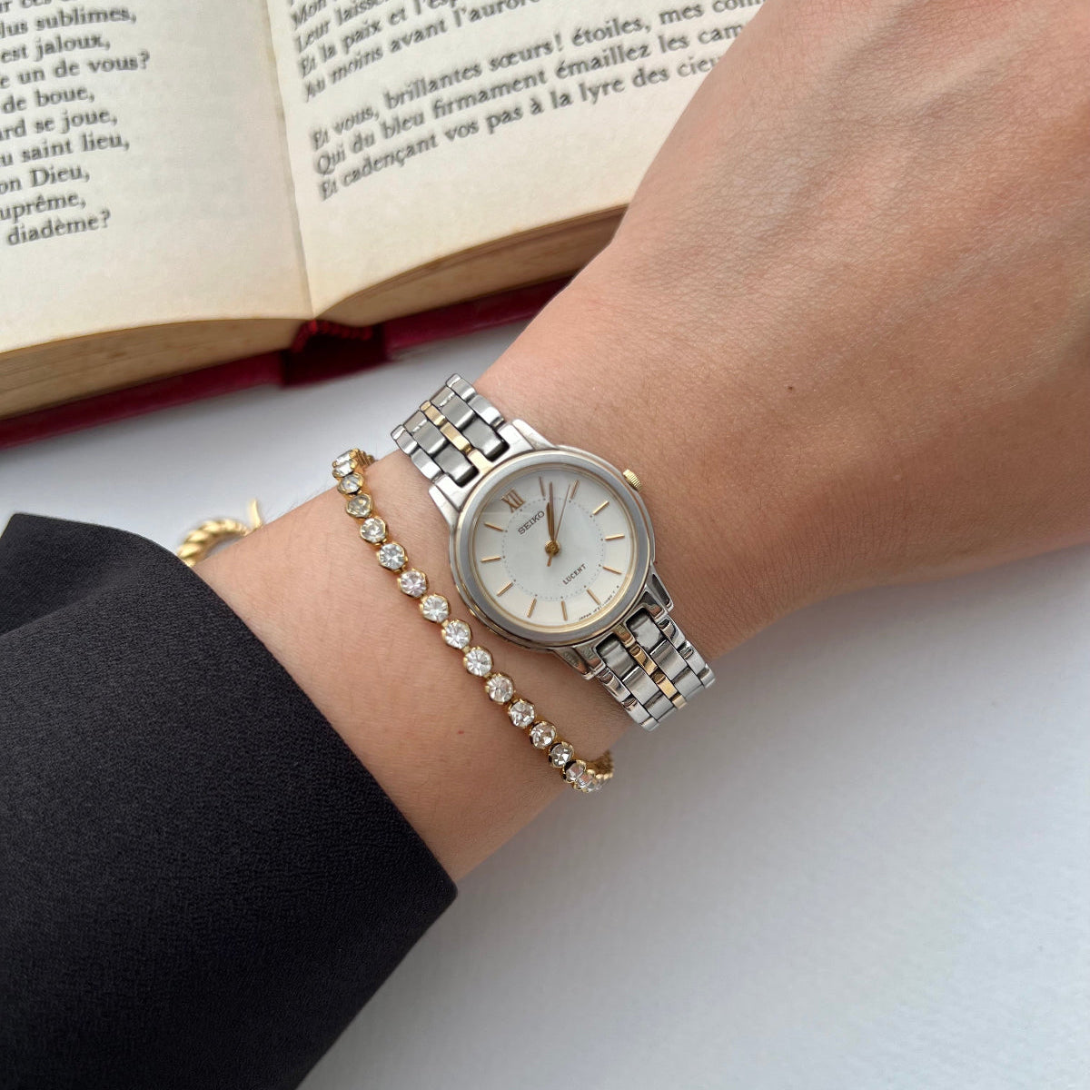 Hand wearing a Seiko Lucent silver women's watch with a book open in the background