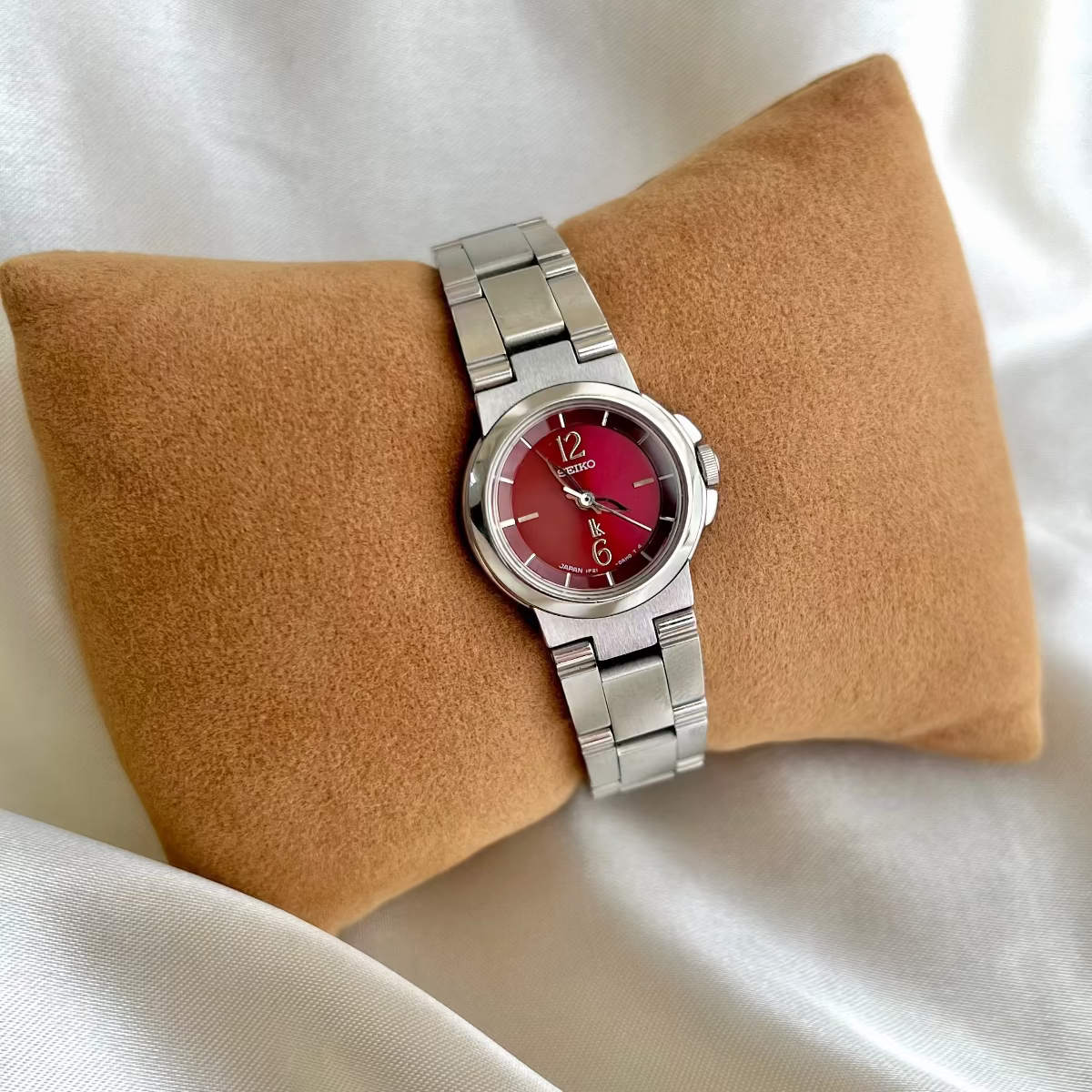 Seiko Lukia silver women's watch with a red face on a beige cushion against a white background