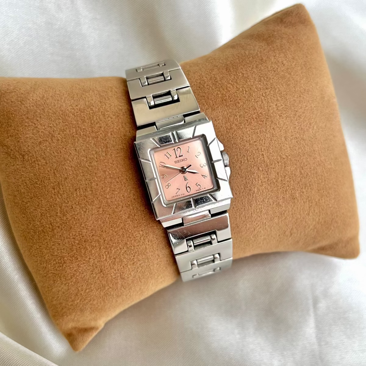 Silver Seiko Luka Women's watch with a pink face on a beige cushion against a white background