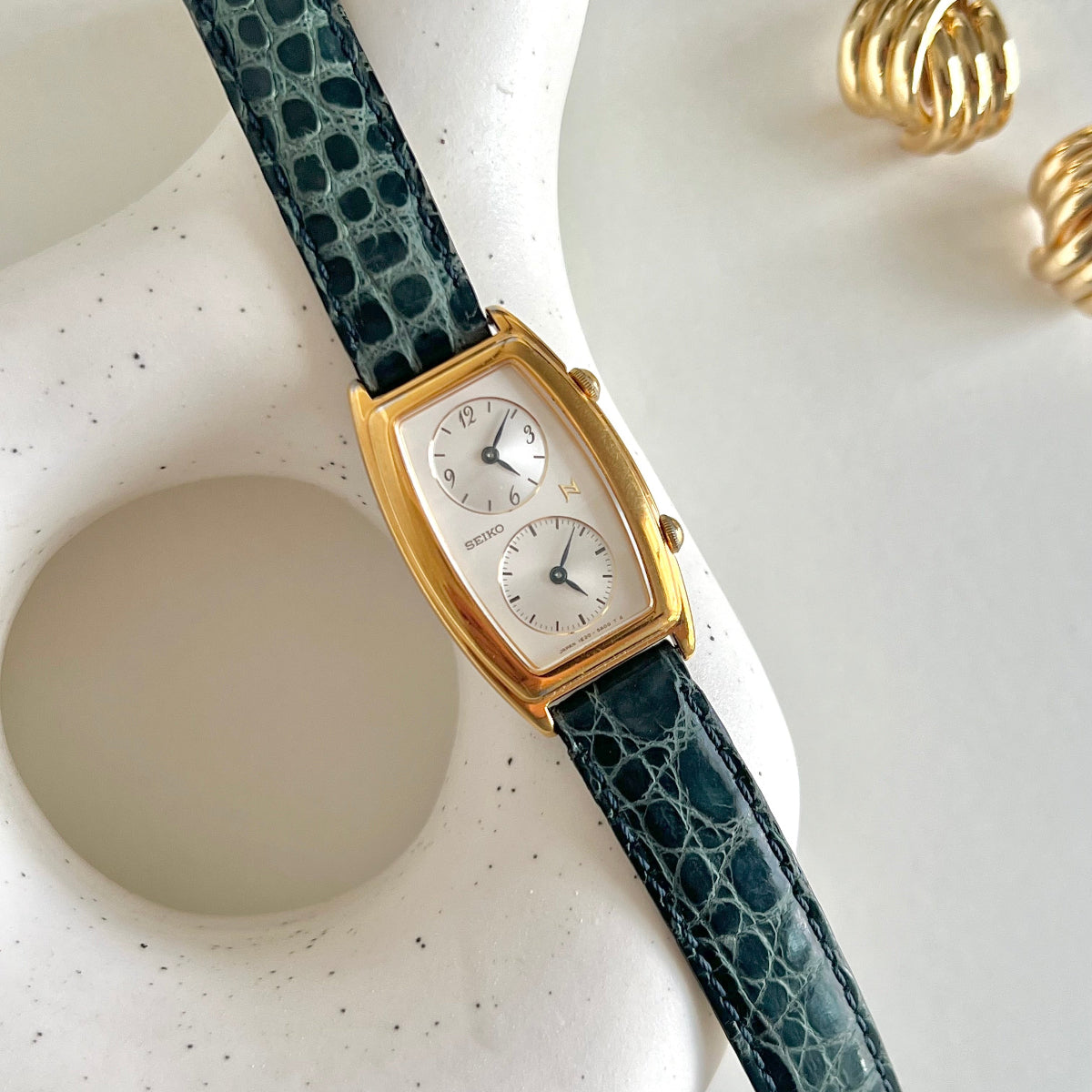 Seiko Noie Dual Dial watch with a green lizard-textured strap on a white surface