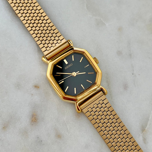 Gold watch with a black face on a marble surface