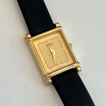 Seiko Gold rectangular watch with black strap on a light gray background