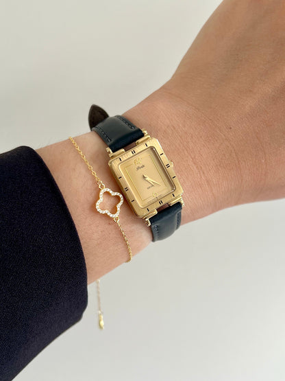 Seiko Gold elegant woman's rectangular watch with black strap on wrist, wearing a gold heart-shaped bracelet.