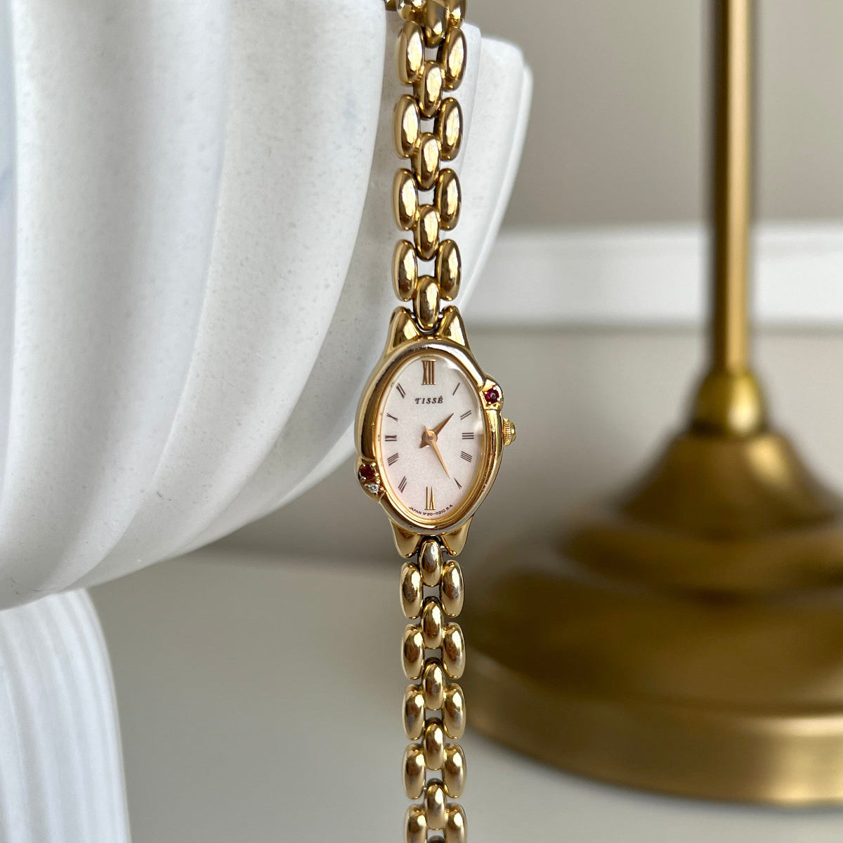 Seiko Tisse Gold Tone chain watch on a white surface with a blurred background with inlaid rubies and diamond