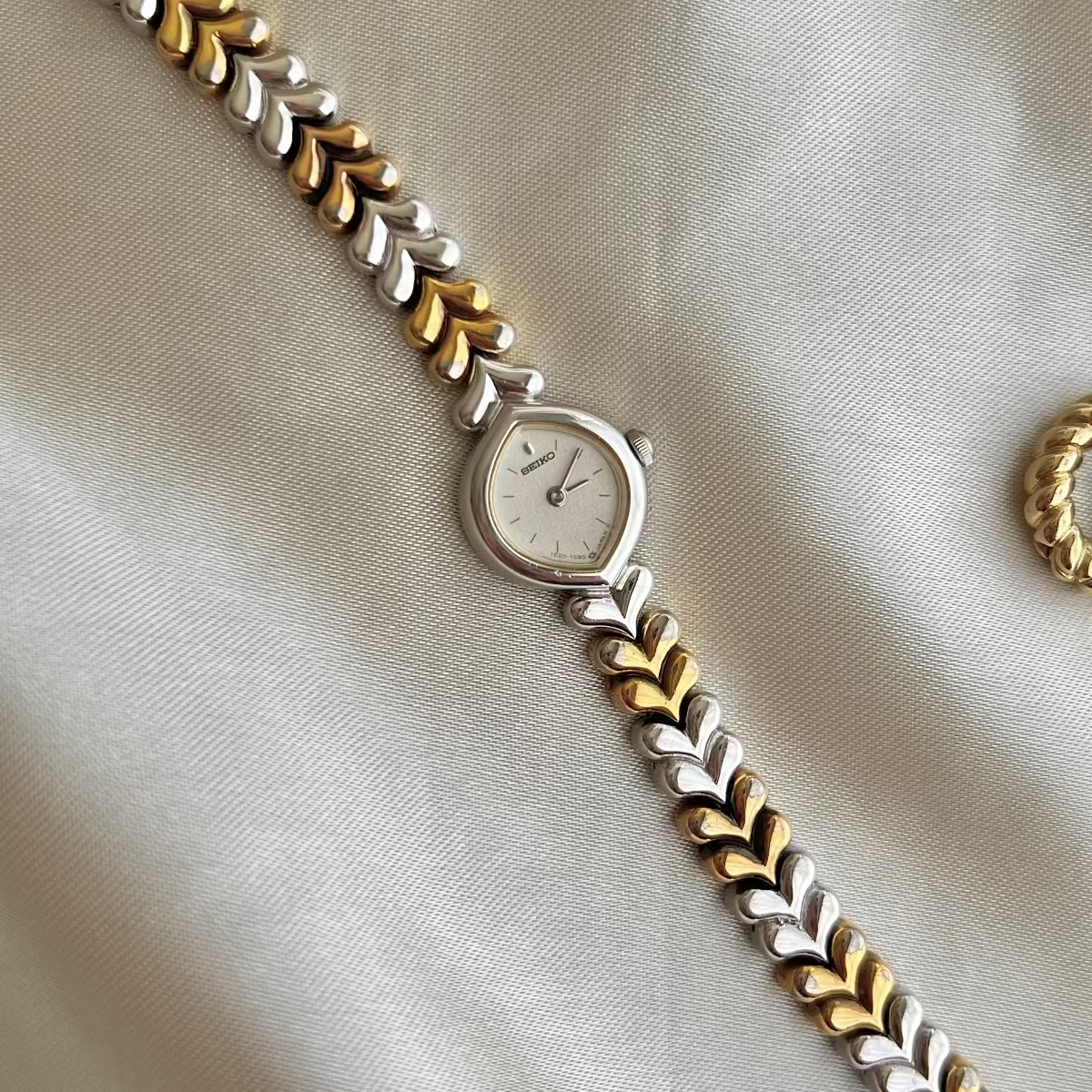 Two-tone Seiko Tisse watch with gold and silver band on a beige fabric background