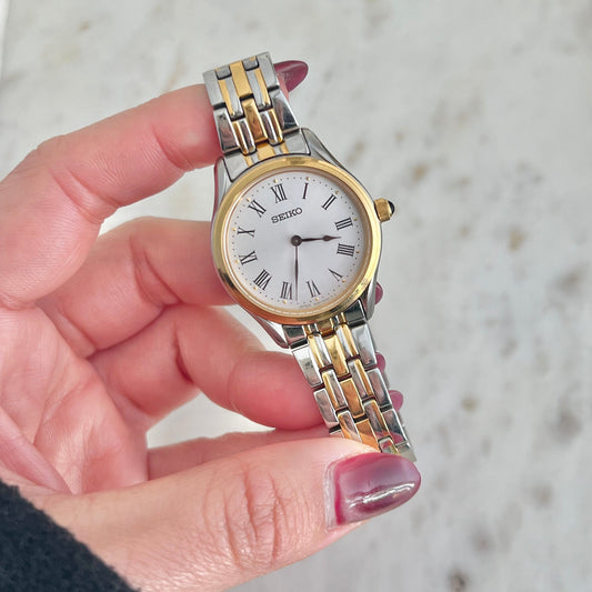 Hand holding a Seiko watch with a two-tone metal band against a neutral background