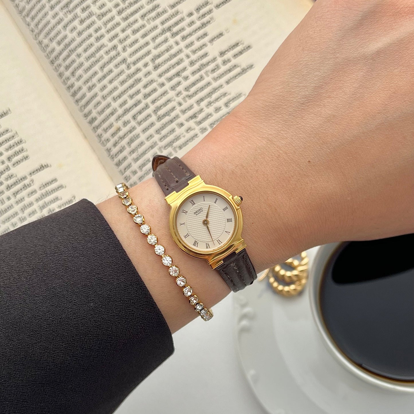 Seiko Gold women's watch on a wrist with a cup of coffee and book in the background