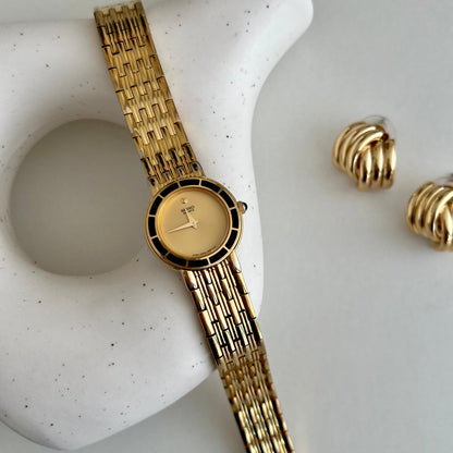 Gold Seiko women's watch and earrings on a textured white surface