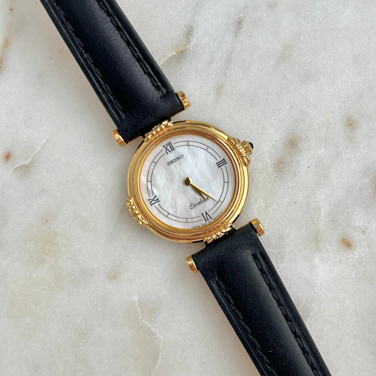Gold Seiko Exceline Pearl Dial watch with black leather strap on a marble surface