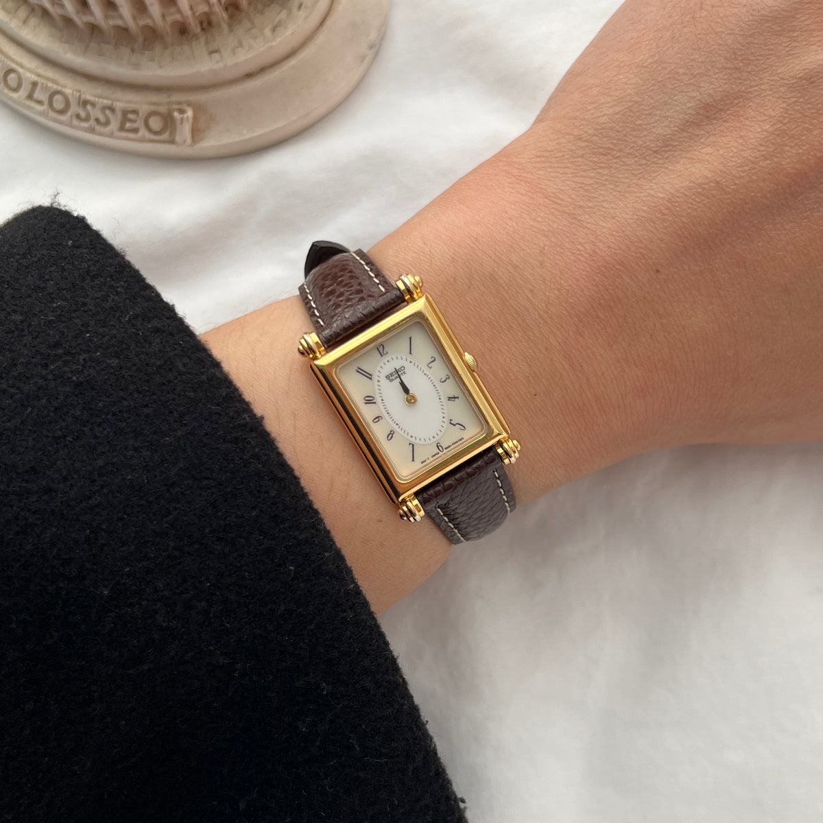 Vintage Seiko women’s watch worn on wrist featuring a gold rectangular case, white dial, black Arabic numerals and brown leather strap