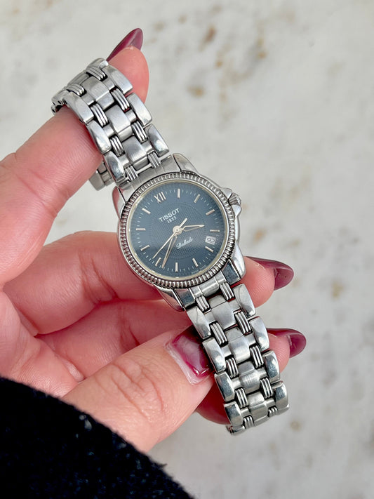 Silver Tissot Ballade watch held by a hand with a blurred background