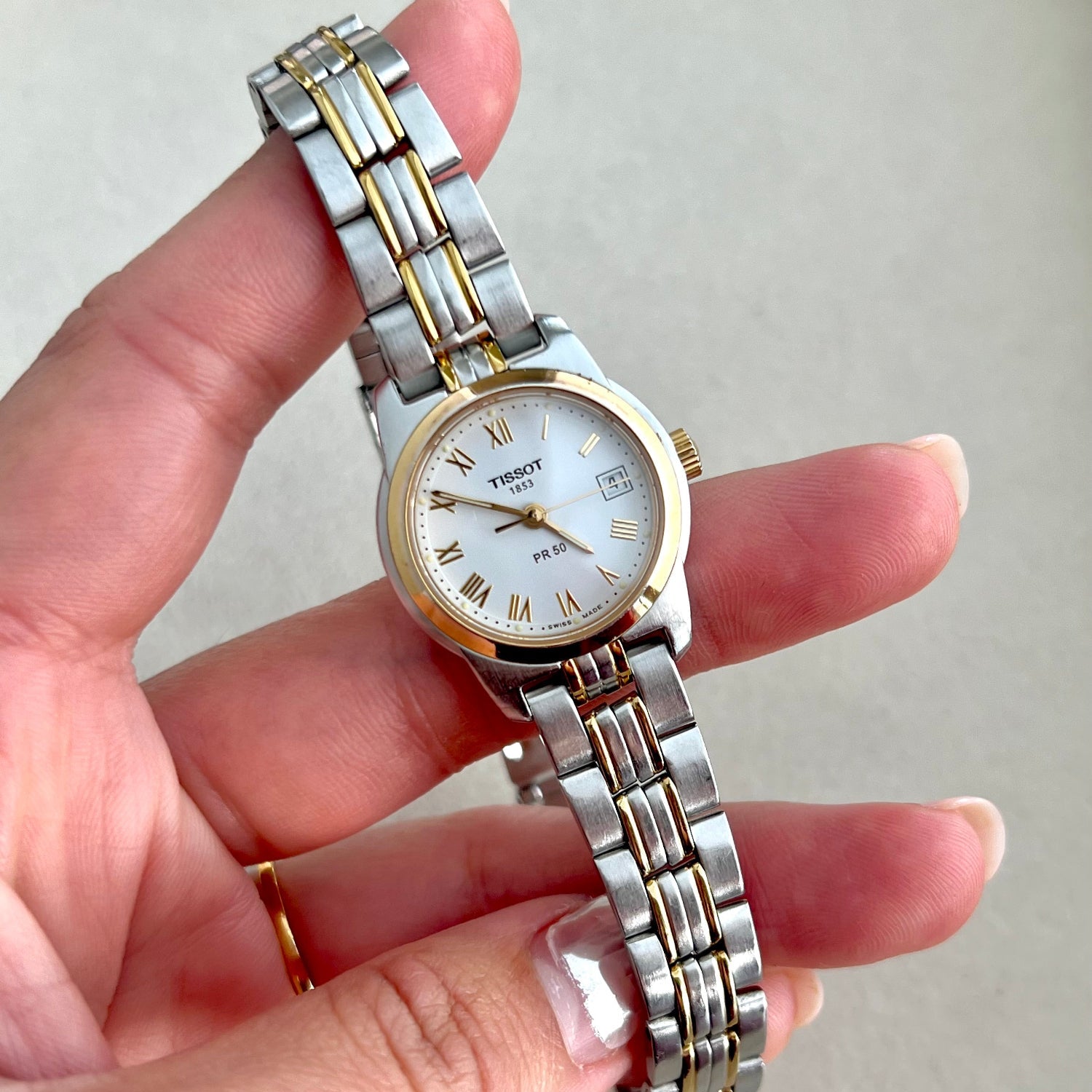 Tissot PR50 Two-tone Women's watch held in a hand against a neutral background