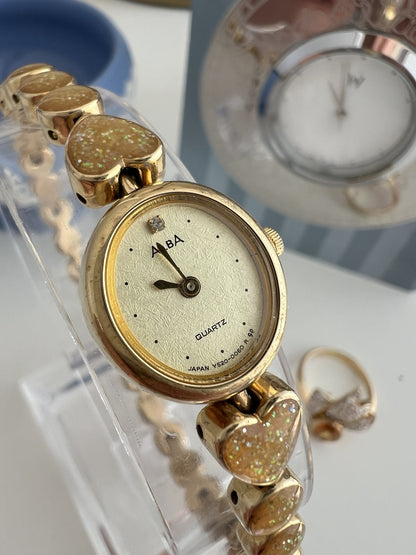 Close view of the Alba champagne textured dial, gold tone oval case and sparkling heart shaped bracelet links.