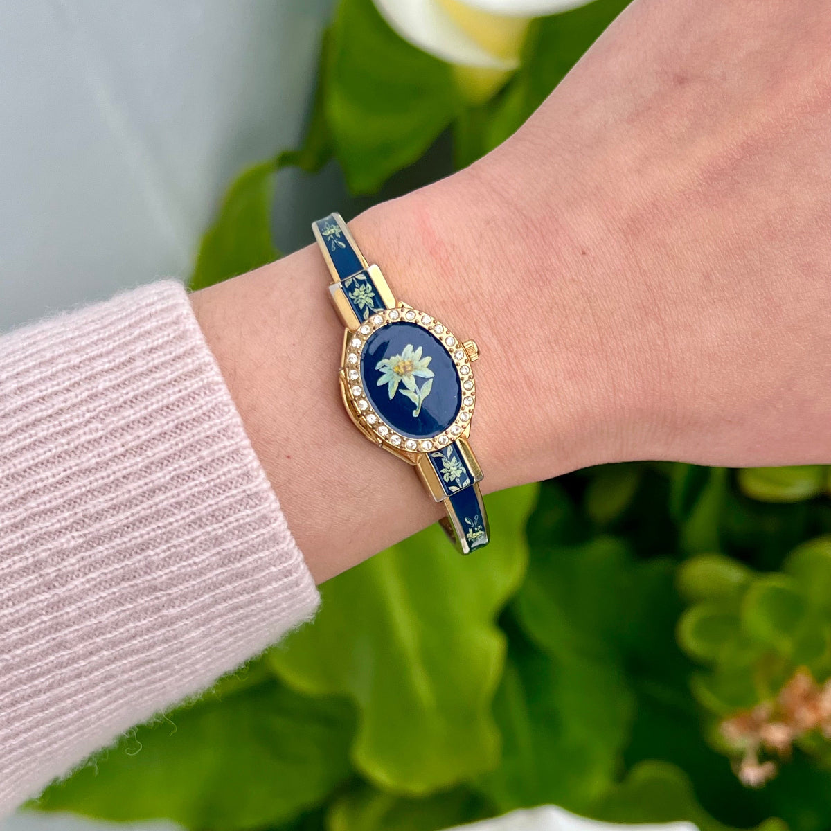 André Mouche Edelweiss women’s secret watch with a dark floral enamel cover, clear crystal border and gold tone bangle.