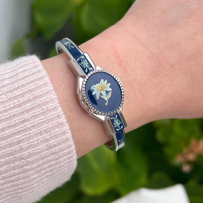 André Mouche Edelweiss women’s bangle watch worn on the wrist, showing its dark floral enamel cover and silver tone border.