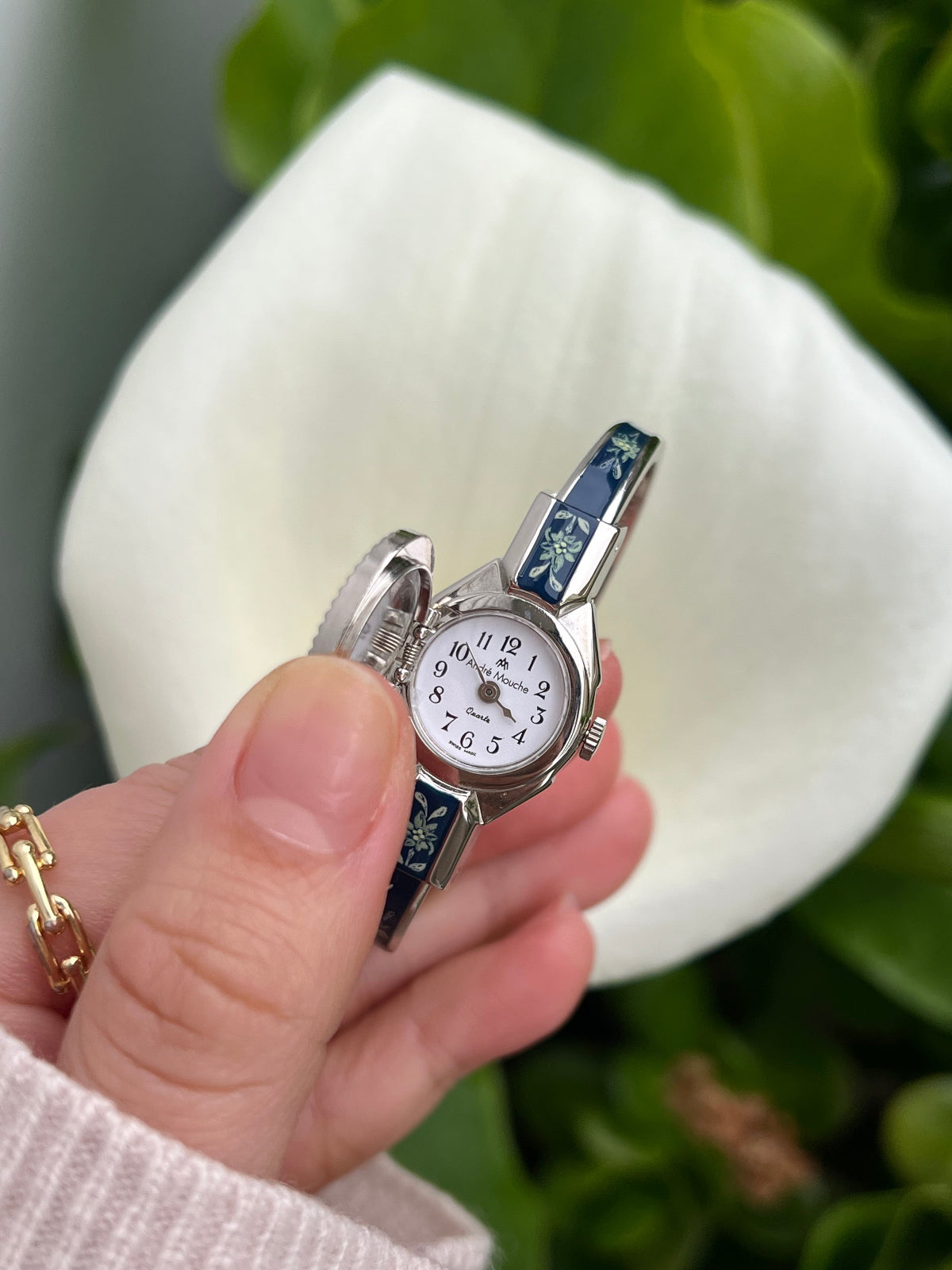 André Mouche Edelweiss secret watch with its floral cover open, revealing a white dial with black Arabic numerals.