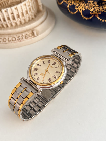 Burberry two tone watch showing the smooth gold tone bezel, silver tone case and bar shaped bracelet connectors.