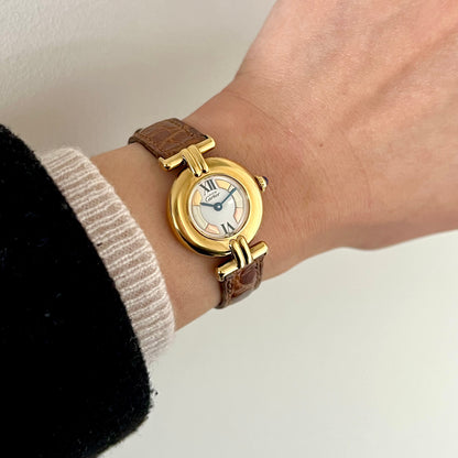 Cartier Colisee Trinity women’s watch worn on wrist with gold round case, segmented pale dial, Roman numerals and brown leather strap