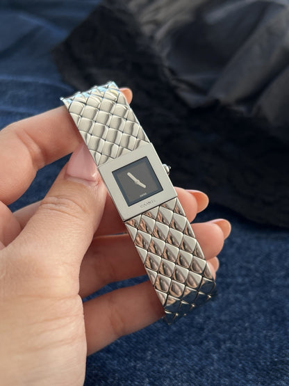 Close view of the Chanel Matelassé black dial, silver tone hands and polished quilted links