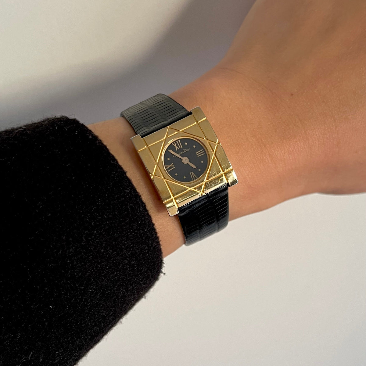 Christian Dior Cannage gold-tone women's watch with a black dial and textured black strap worn on the wrist