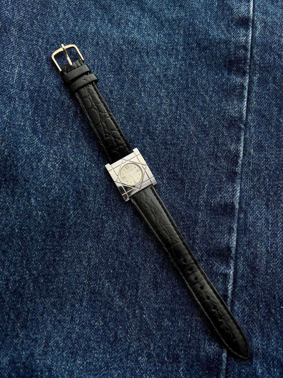 Christian Dior Cannage women’s square steel watch with silver Roman dial and black leather strap arranged on denim