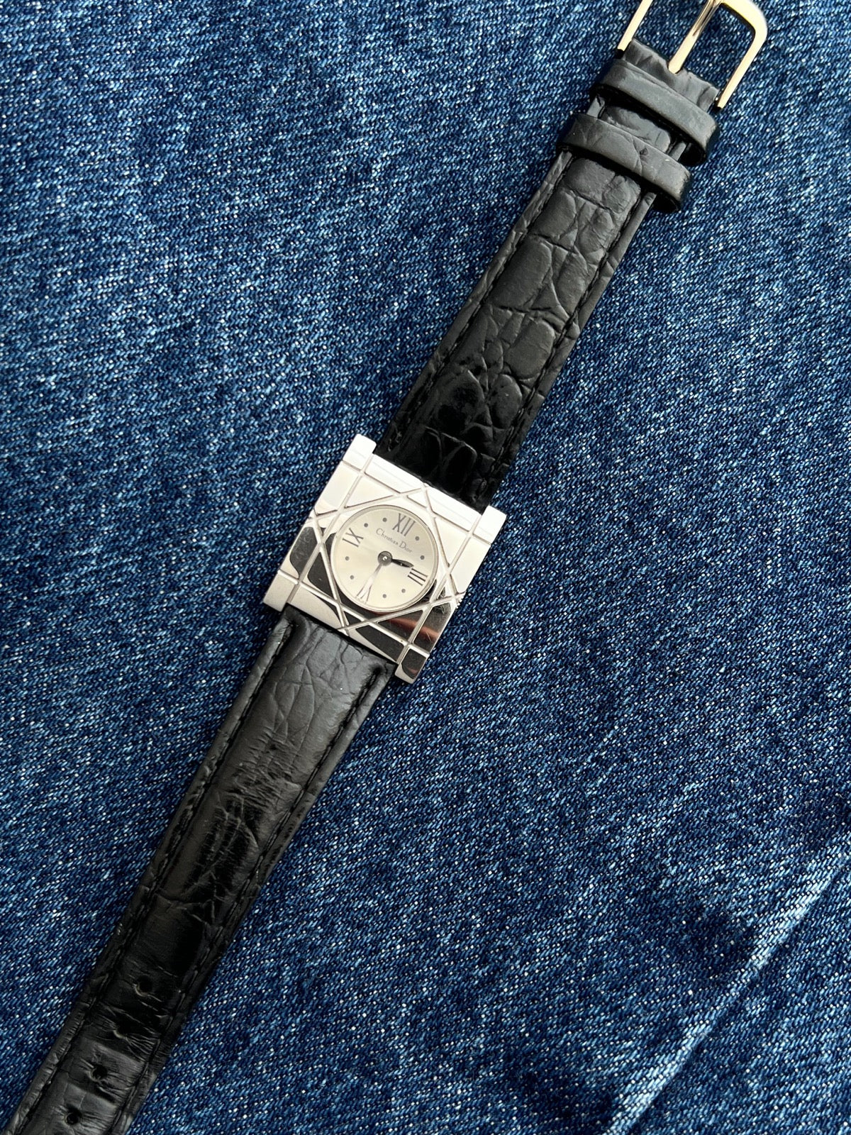 Full view of the Christian Dior Cannage women’s steel watch with black leather strap and gold tone buckle on denim
