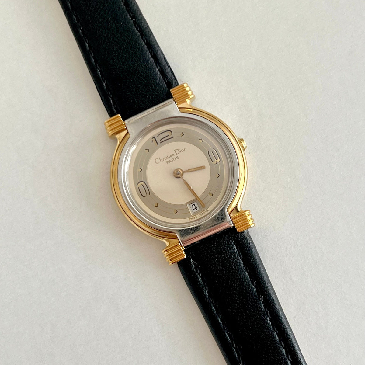 Christian Dior gold tone women’s watch with layered dial, black leather strap, and date window
