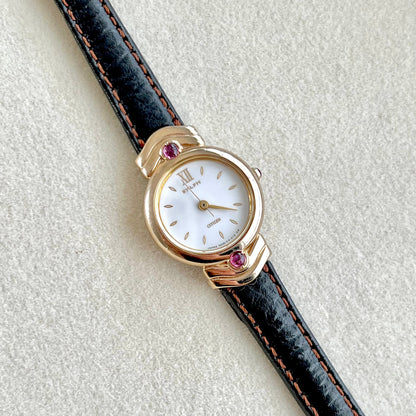 Citizen women’s watch with a gold-tone case set with purple gemstones, white dial, and leather strap with red stitching. (Citizen Sylph model).