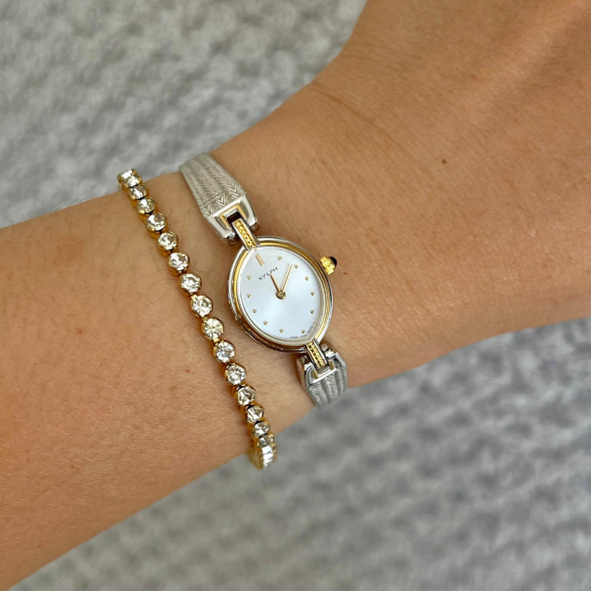 Citizen Sylph oval watch with blue cabochon crown and two-tone bracelet shown on a wrist.