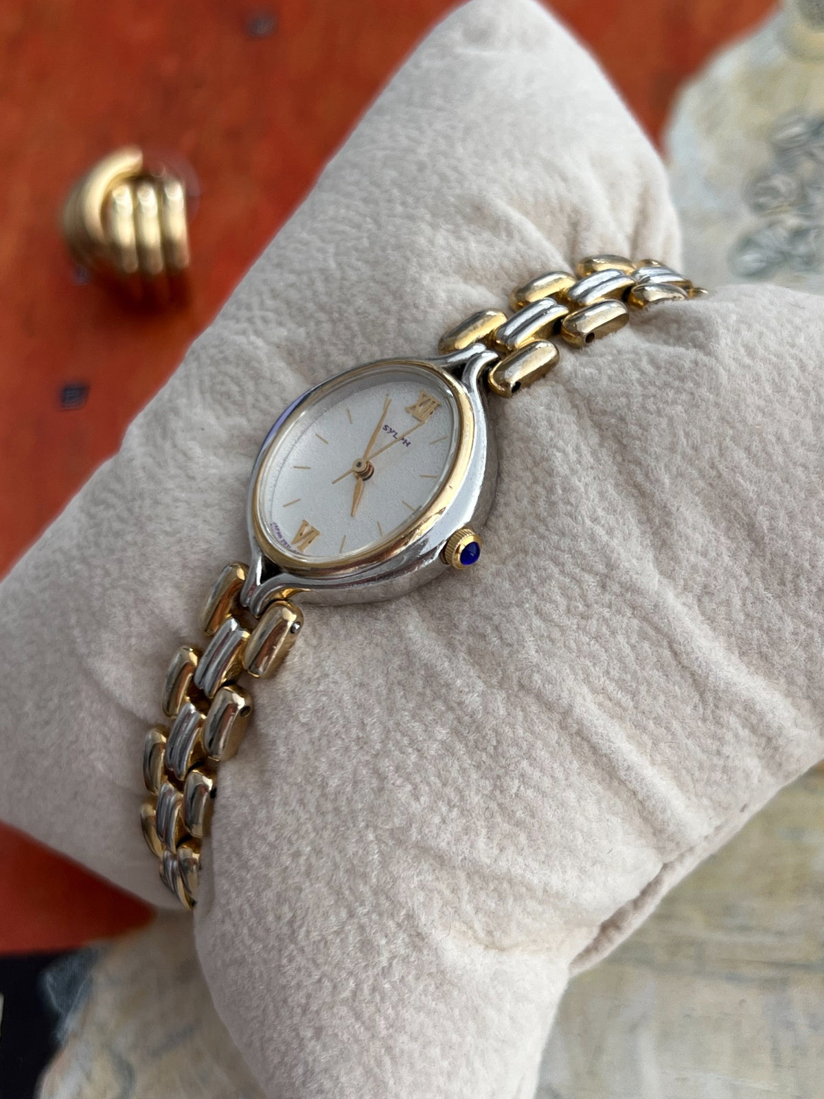 Citizen Sylph oval watch showing its blue cabochon crown, gold tone inner bezel and polished silver tone case
