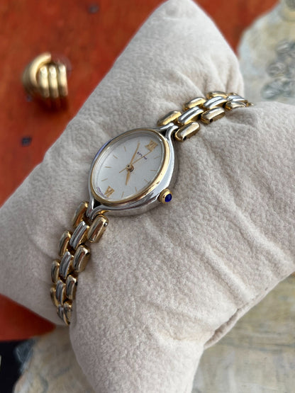 Citizen Sylph oval watch showing its blue cabochon crown, gold tone inner bezel and polished silver tone case