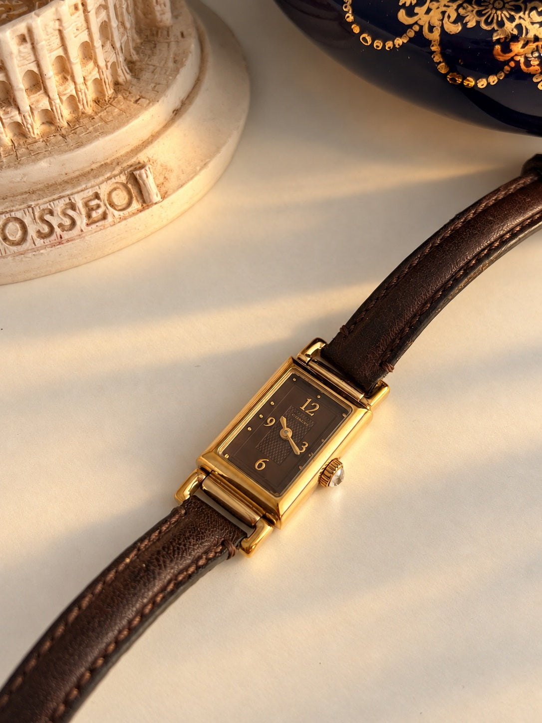Coach women’s watch with chocolate brown Arabic numeral dial, rectangular gold tone case and brown leather strap