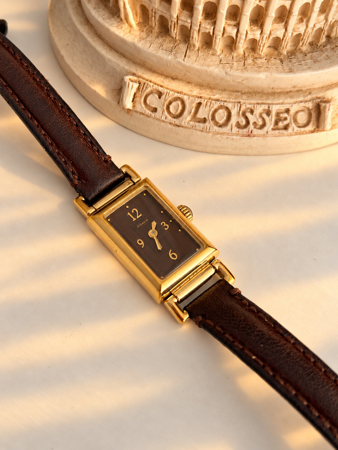 Coach chocolate brown dial tank women’s watch with gold Arabic numerals, narrow gold tone case and brown leather strap