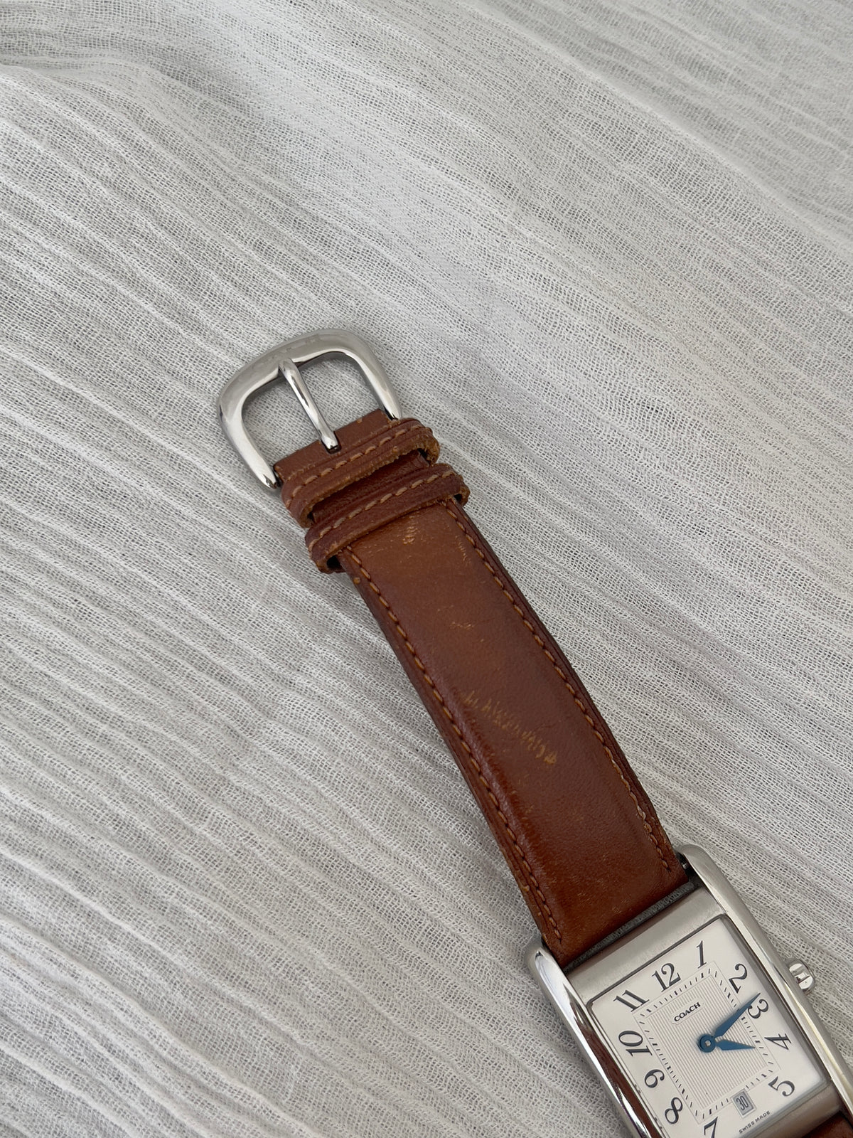Side profile of the polished rectangular case on a Coach watch.
